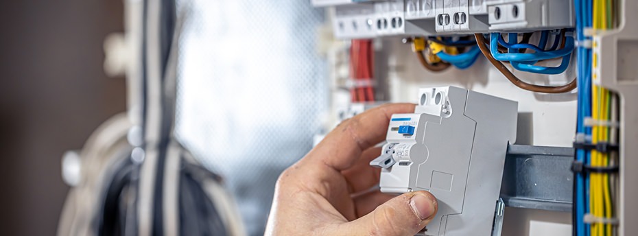 Blick in ein Elektro Tableau auf eine Hutschiene bei der ein Elektriker gerade eine Komponente einklickt